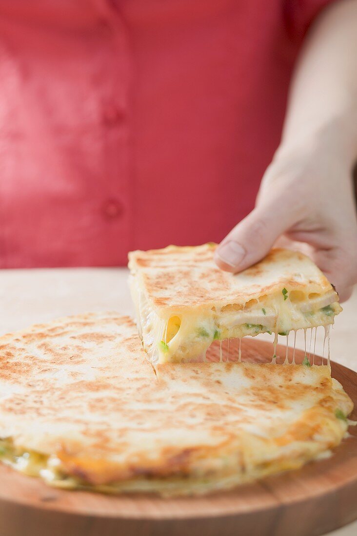 Hand nimmt Stück Quesadilla vom Holzteller