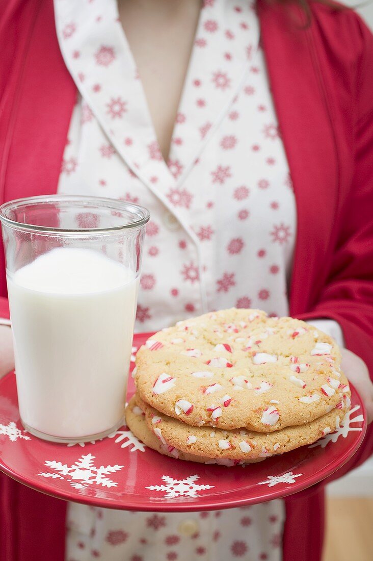 Frau hält Teller mit Weihnachtscookies und Glas Milch