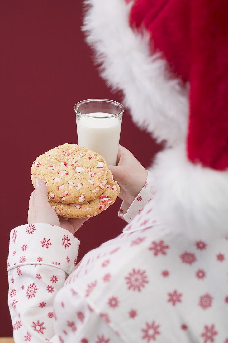 Frau mit Nikolausmütze hält Weihnachtscookies und Glas Milch