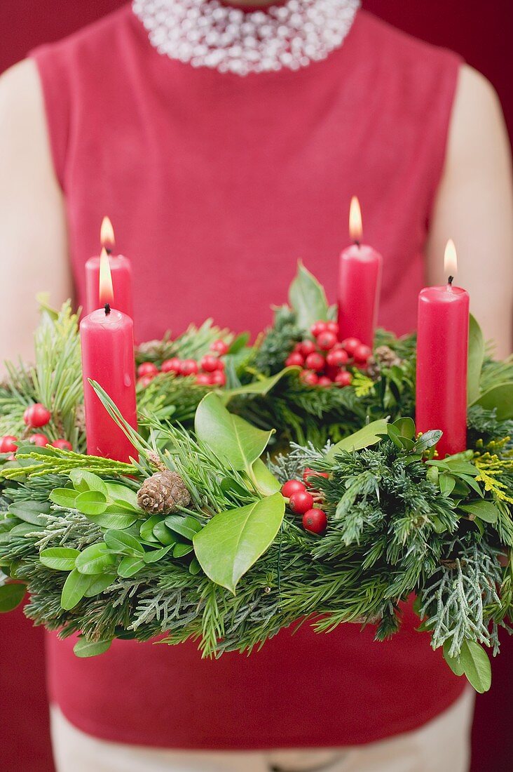 Woman holding Advent wreath with four burning candles