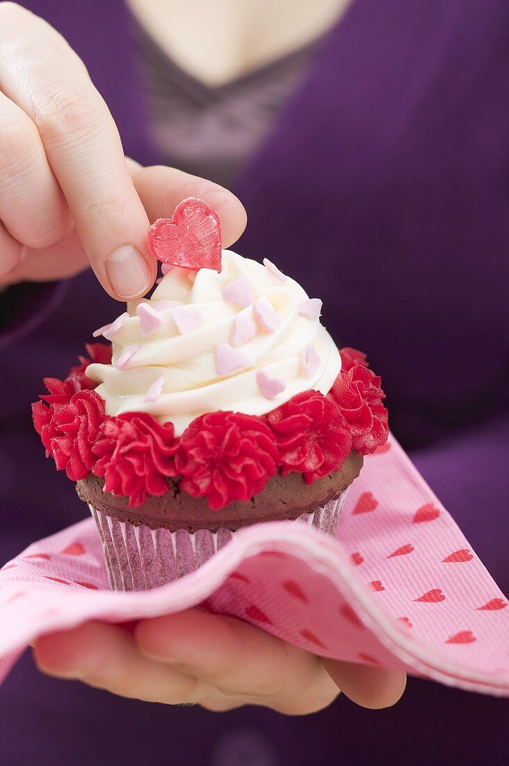 Frau hält Cupcake zum Valentinstag auf Papierserviette