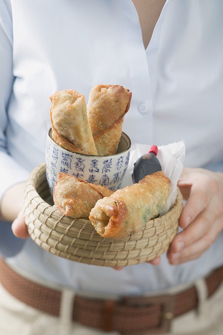 Woman holding basket of spring rolls and soy sauce