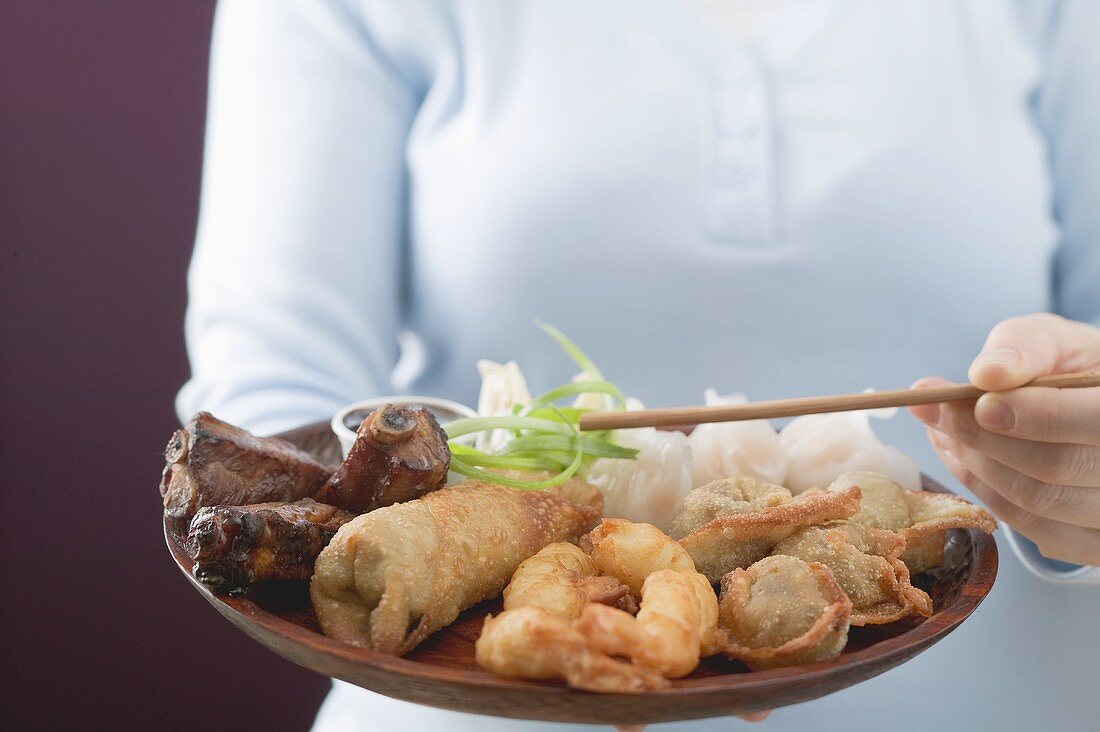 Woman holding Asian appetiser platter and chopsticks