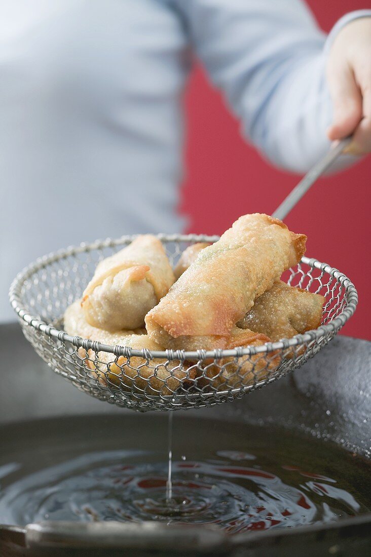 Taking deep-fried spring rolls out of wok