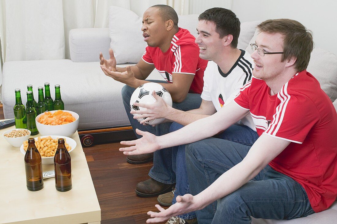 Drei Fussballfans mit Knabberzeug und Bier beim Fernsehen
