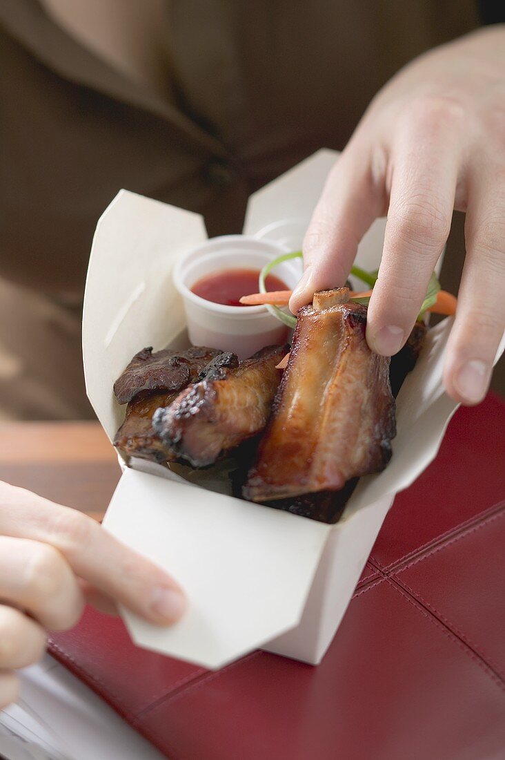 Woman taking glazed pork rib out of take-away container