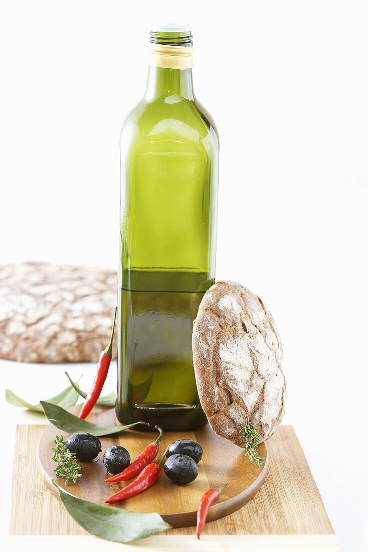 Flasche Olivenöl, Oliven, Chilischoten und rustikales Brot