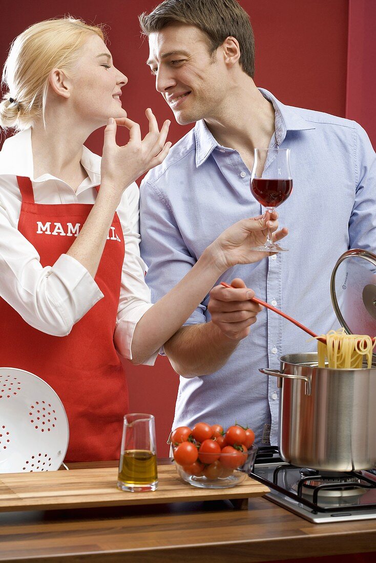 Paar kocht Spaghetti mit Tomaten, Frau hält Glas Rotwein