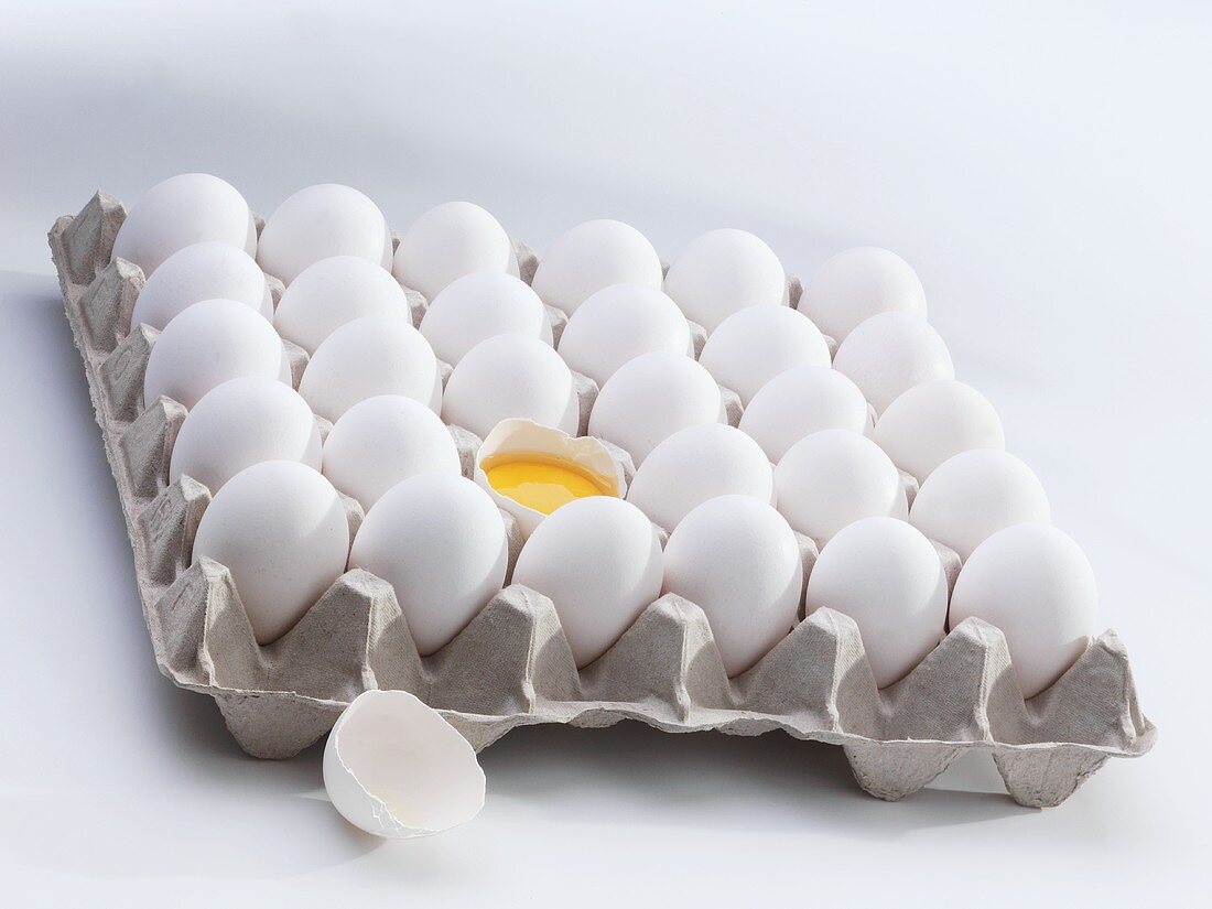 Frische Eier im Eierkarton, eines aufgeschlagen
