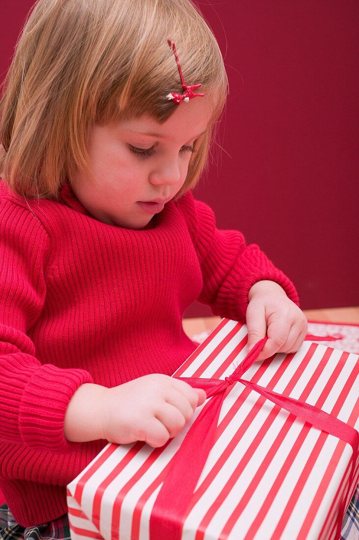 Kleines Mädchen öffnet Schleife am Weihnachtspaket