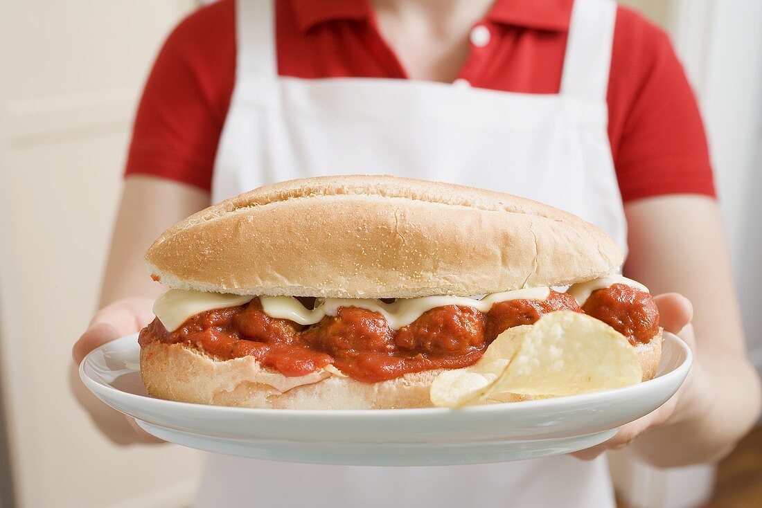 Woman holding giant sandwich filled with meatballs & tomato sauce