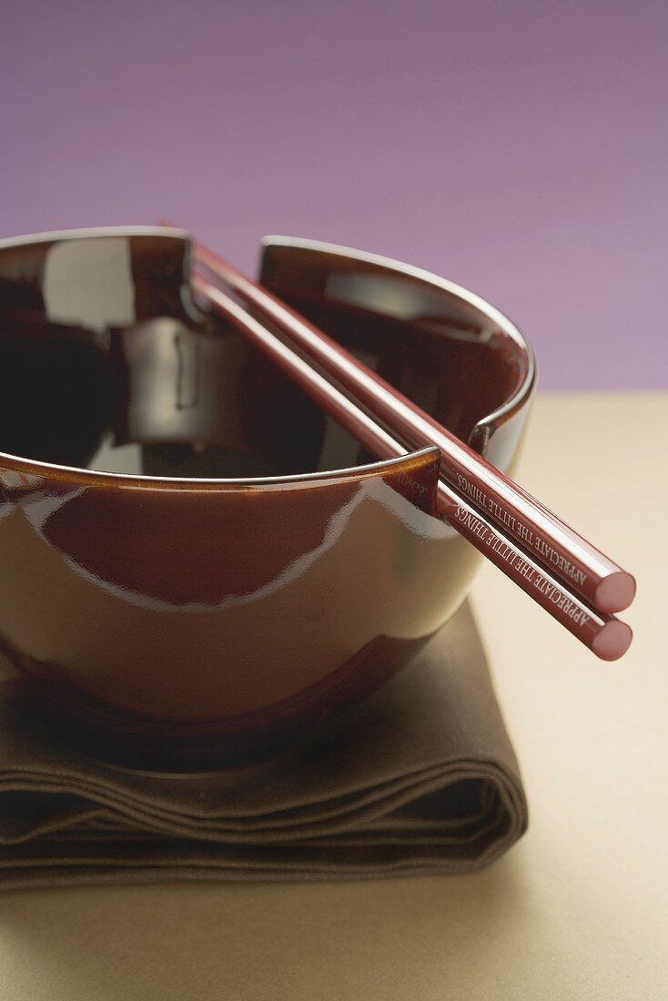 Lacquer bowl with chopsticks on brown cloth (Asia)