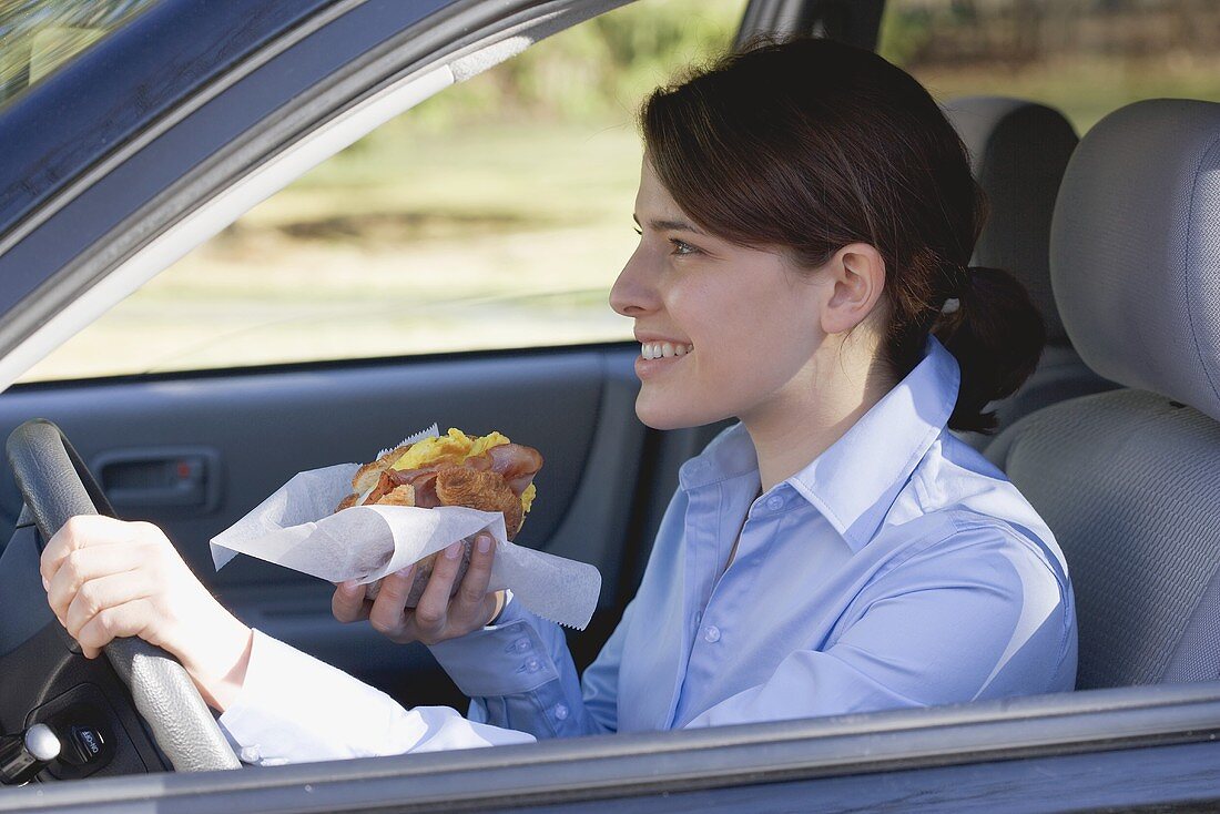 Junge Frau isst Croissant beim Autofahren