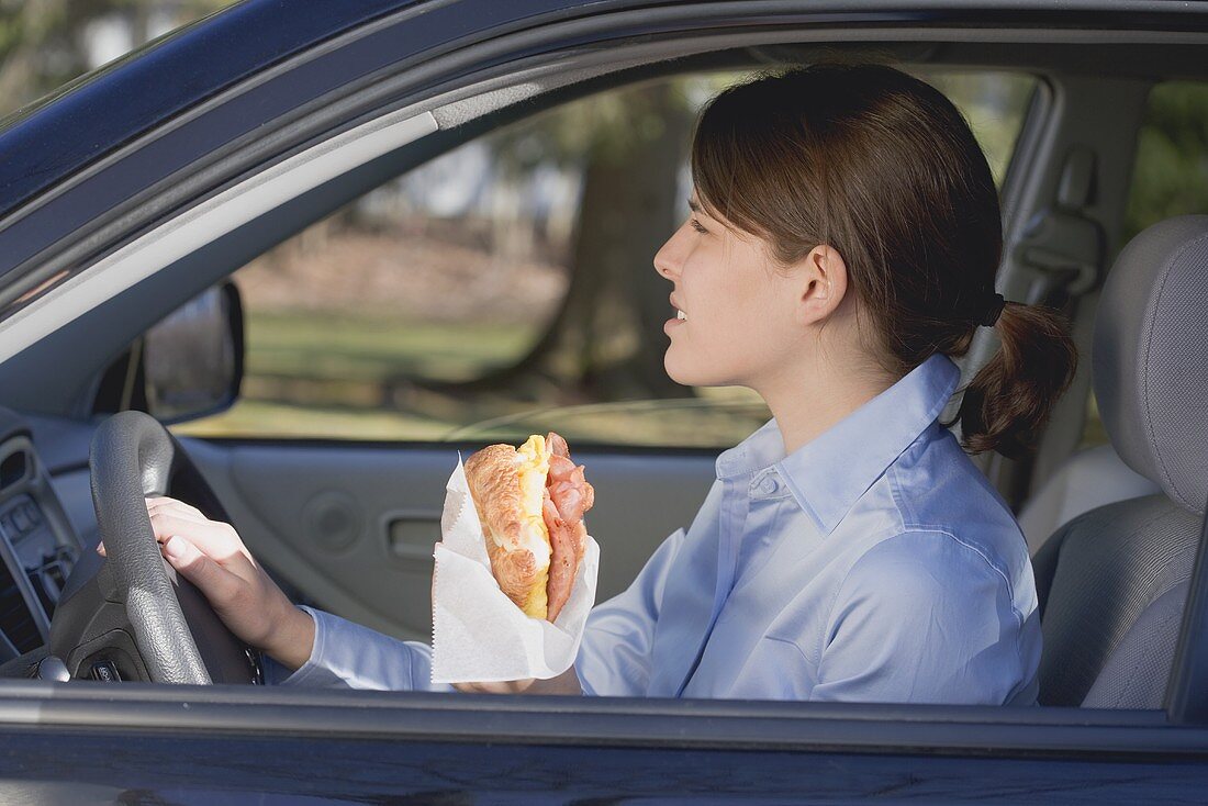 Junge Frau isst Croissant im Auto