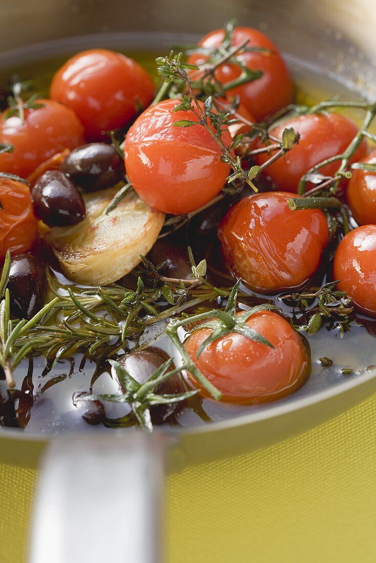 Fried cherry tomatoes with garlic and olives in frying pan