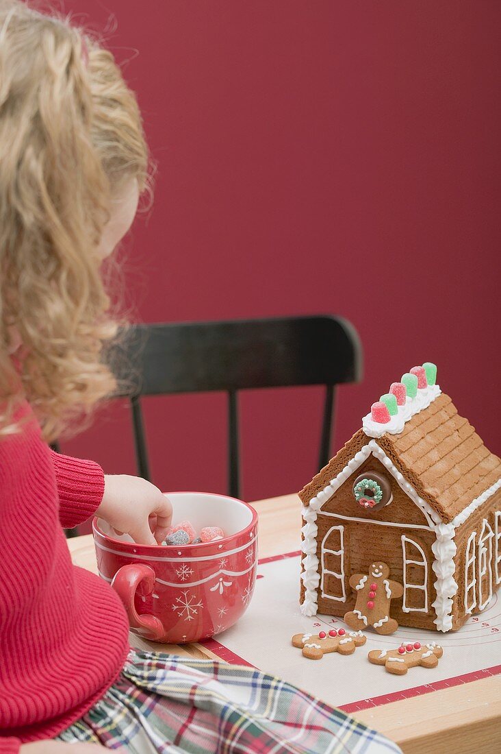 Kleines Mädchen verziert Lebkuchenhaus mit Geleebonbons