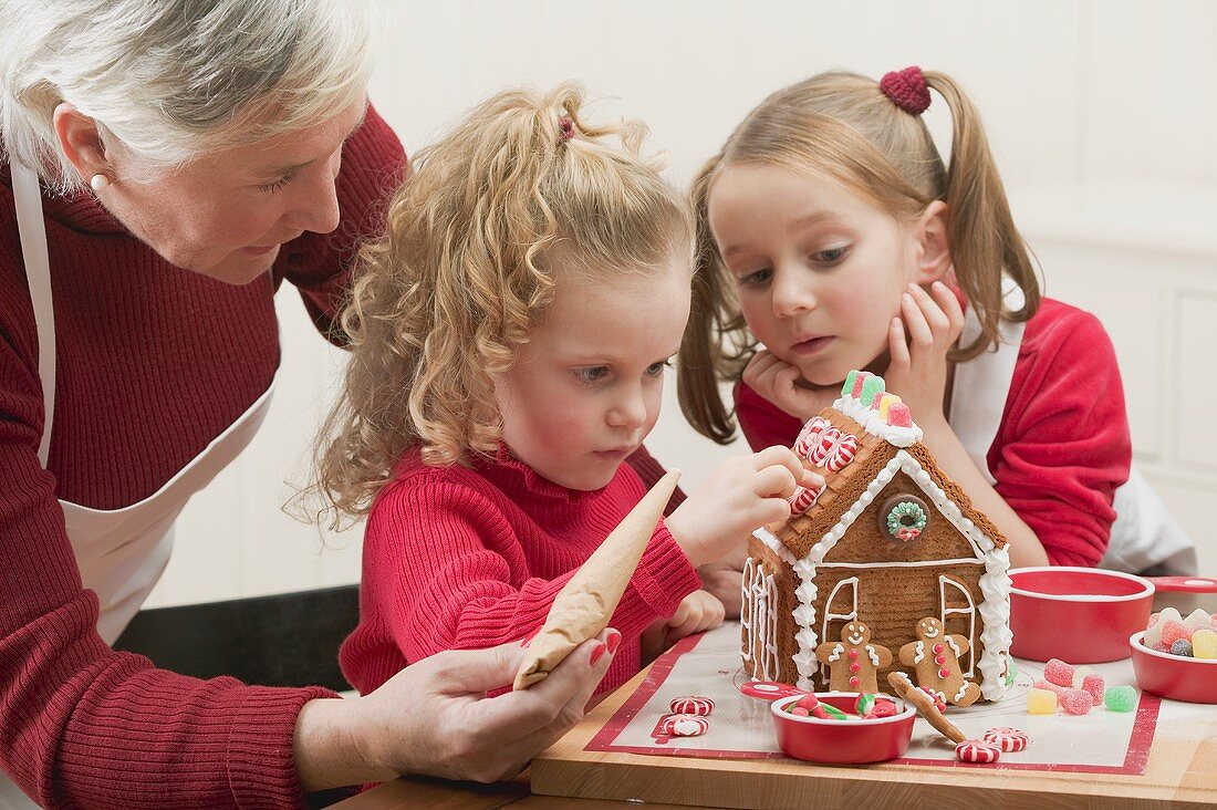 Kleine Mädchen verzieren mit Grossmutter Lebkuchenhaus