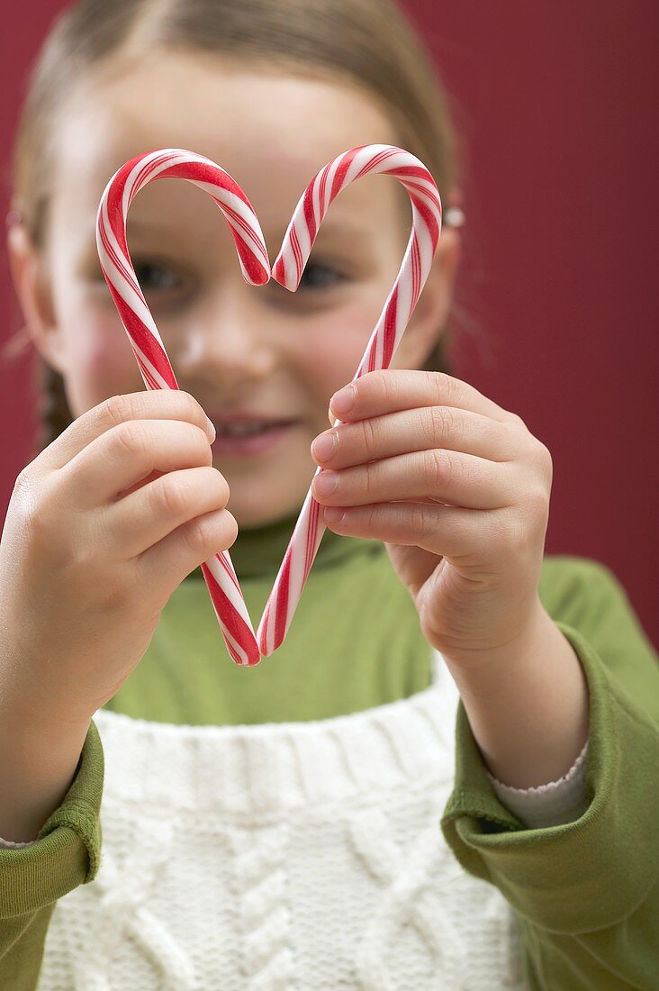 Small girl looking through heart made from two candy canes