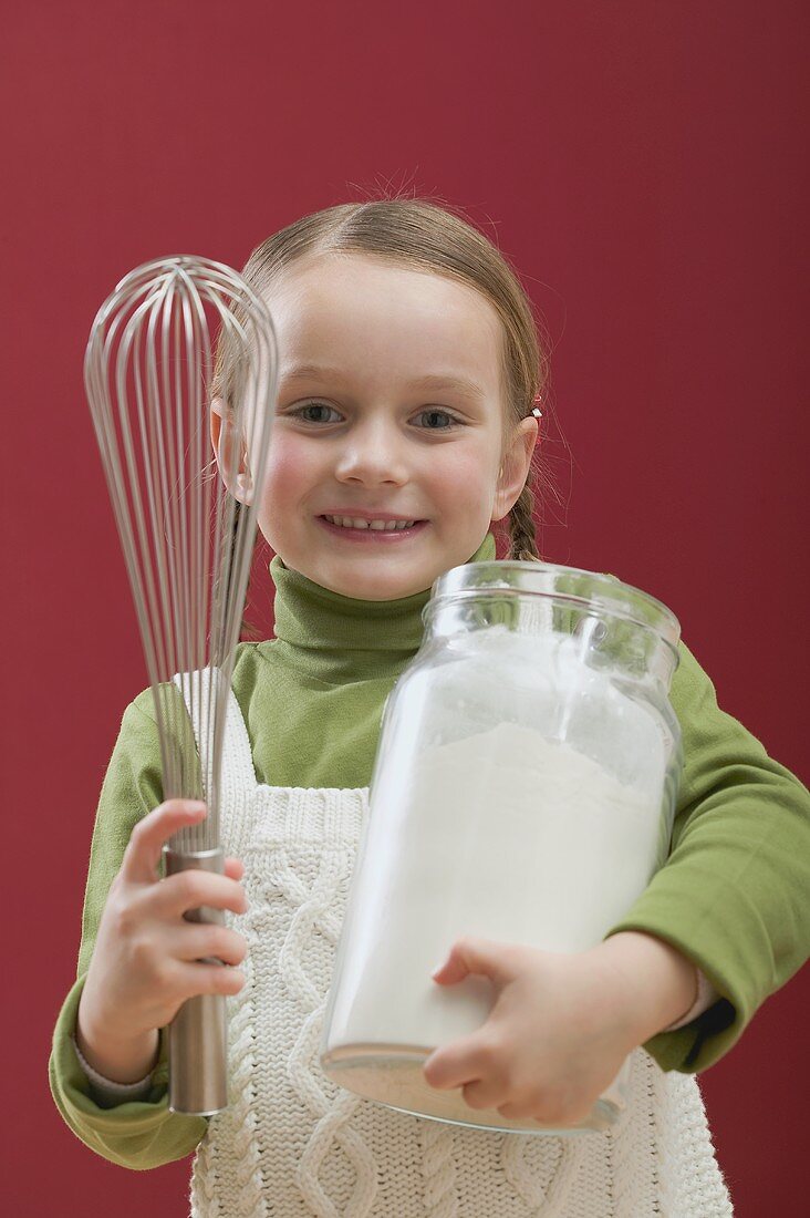 Small girl holding large jar of flour and whisk