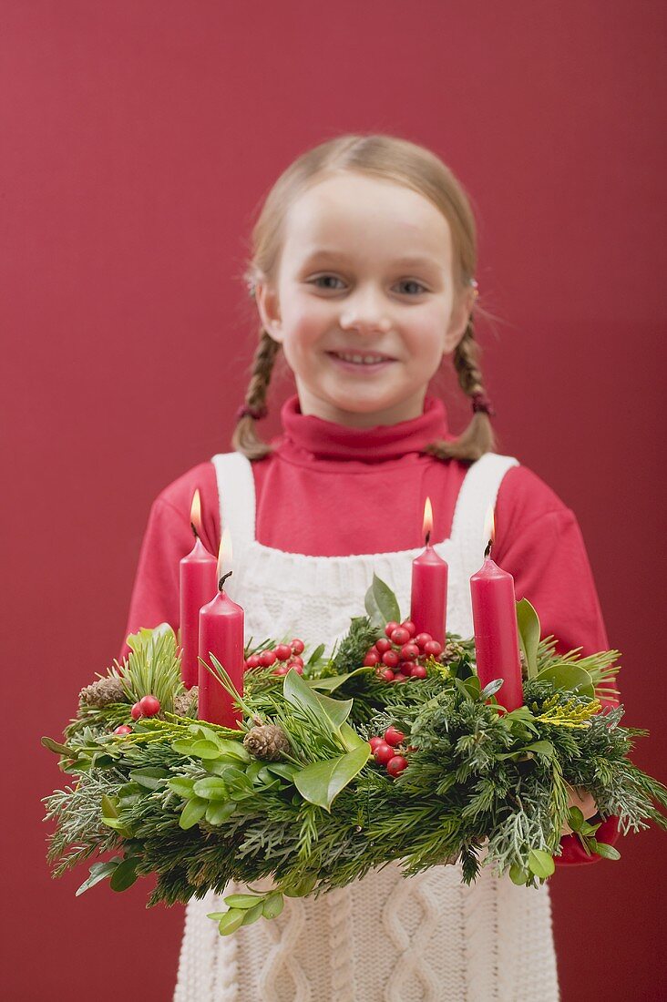 Kleines Mädchen hält Adventskranz mit brennenden Kerzen