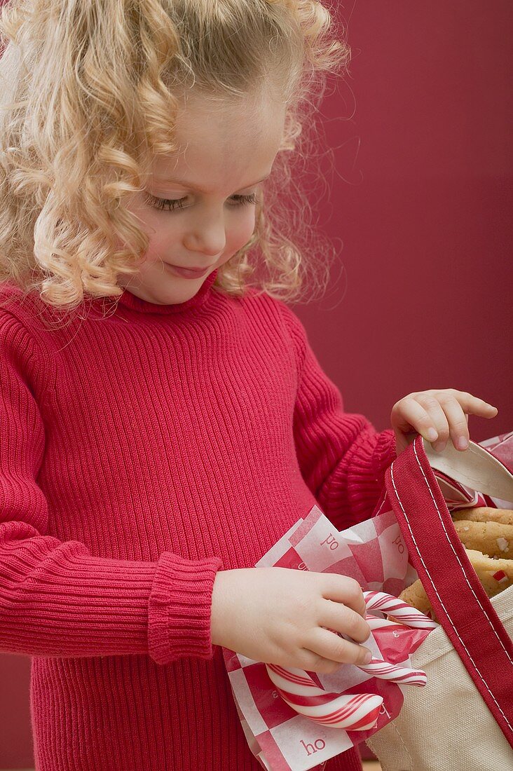 Kleines Mädchen hält Tasche mit Zuckerstangen und Plätzchen