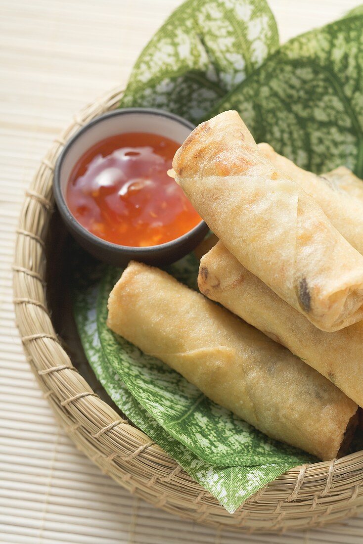 Spring rolls and chilli sauce on leaves in basket