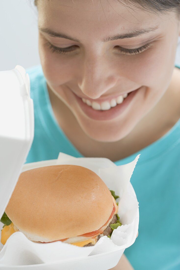 Junge Frau betrachtet Cheeseburger in geöffneter Verpackung