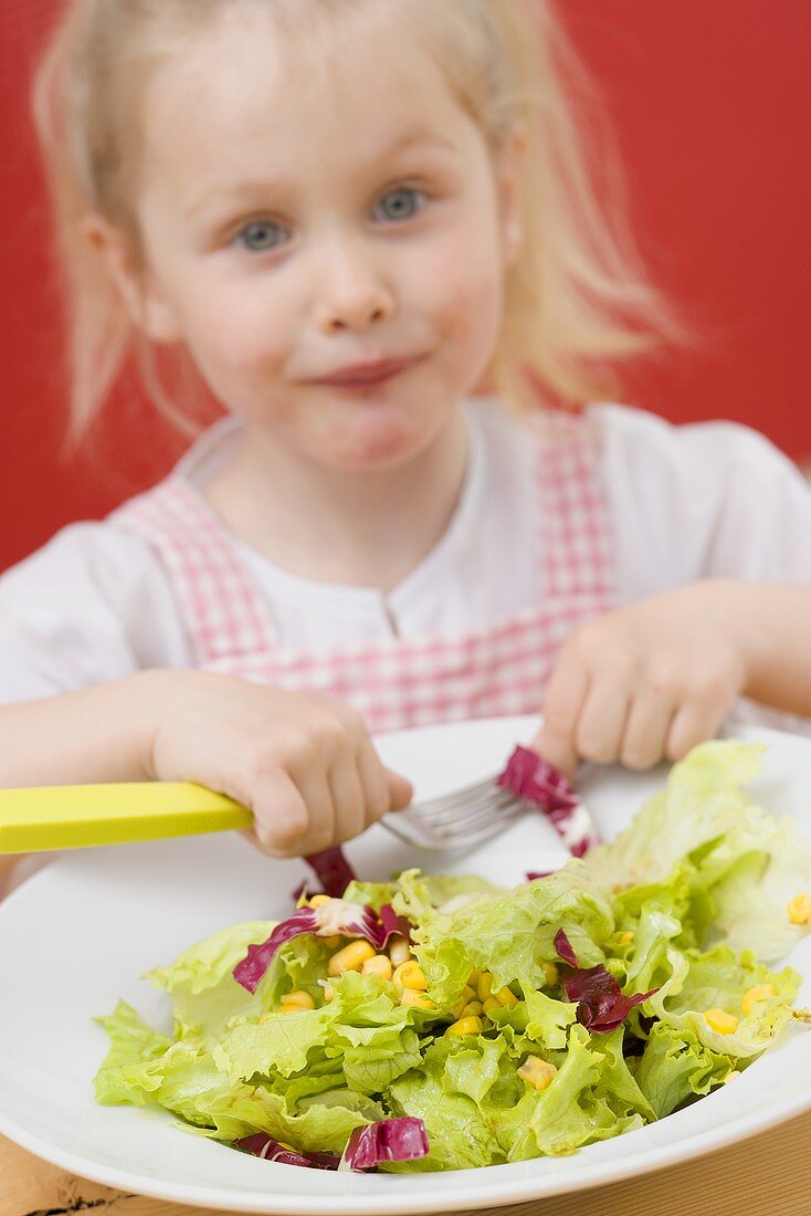 Kleines Mädchen isst Blattsalat mit Mais