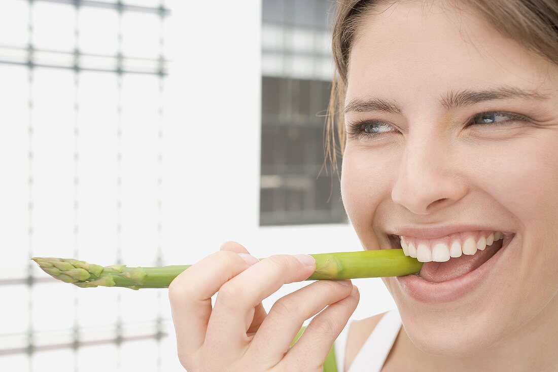 Young woman biting into a spear of green asparagus