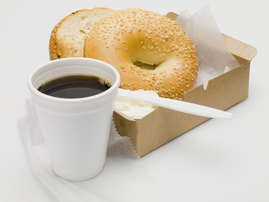 Sesame bagel with crème fraîche in cardboard box, cup of coffee