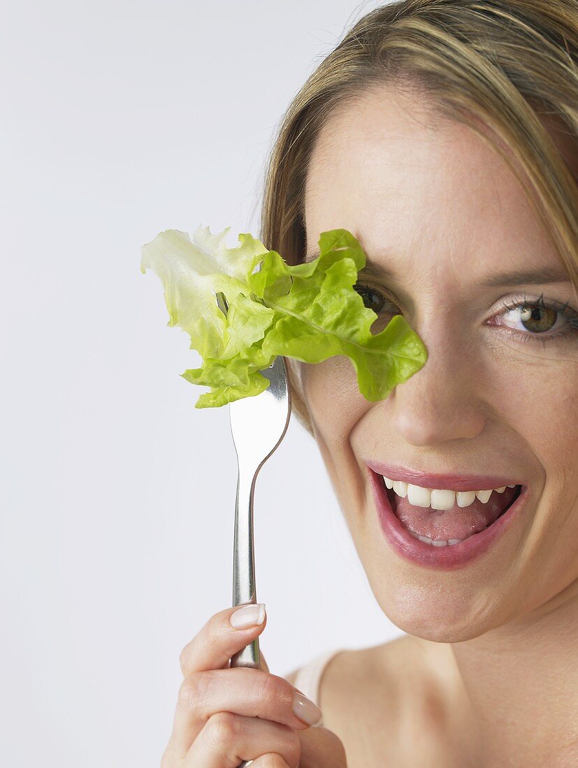 Woman holding lettuce leaf on fork in front of her eye
