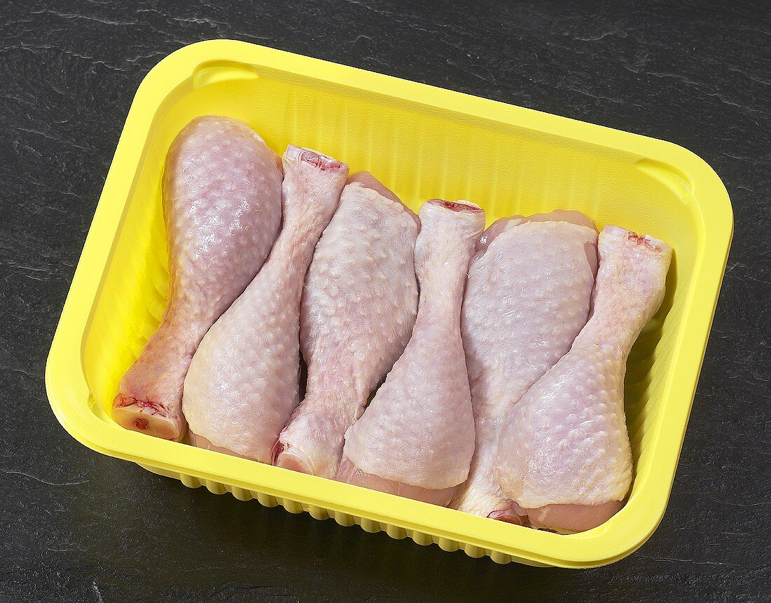 Fresh chicken drumsticks in plastic container