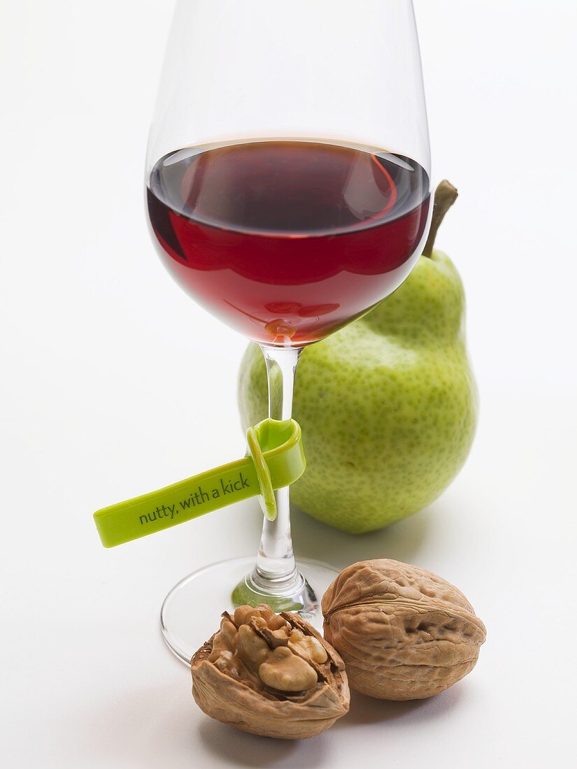 Glass of red wine with plastic label, walnuts and pear