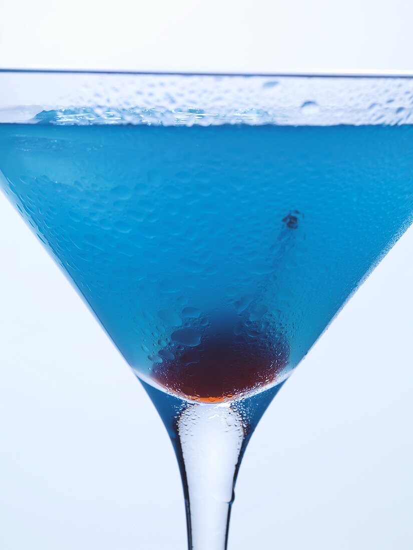 Blue Curaçao cocktail with cocktail cherry (close-up)