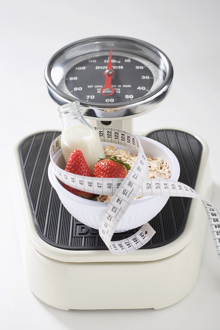 Strawberries, milk, cereal and tape measure on scales