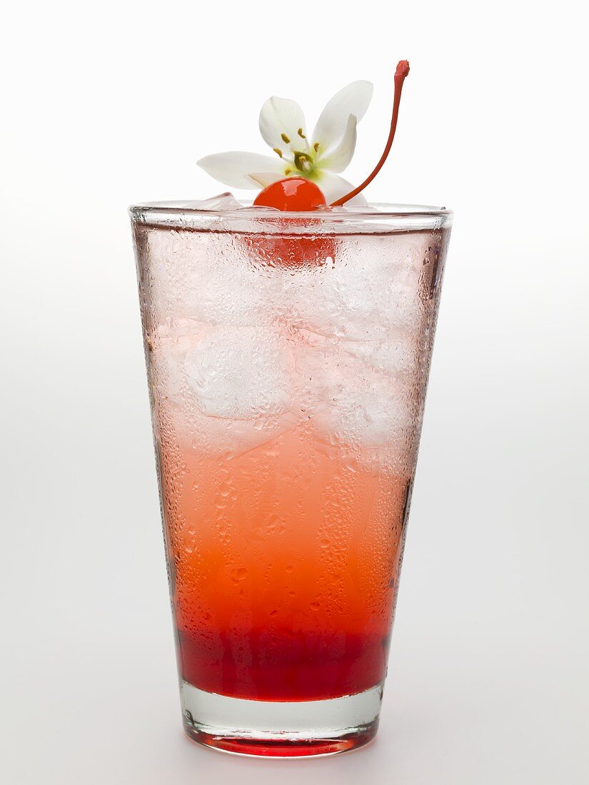 Tequila Sunrise with ice cubes, cocktail cherry and flower