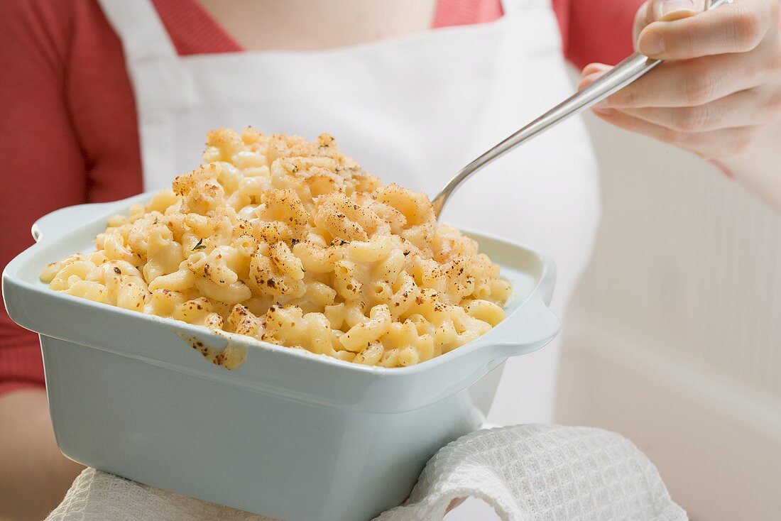 Woman holding baking dish of macaroni cheese