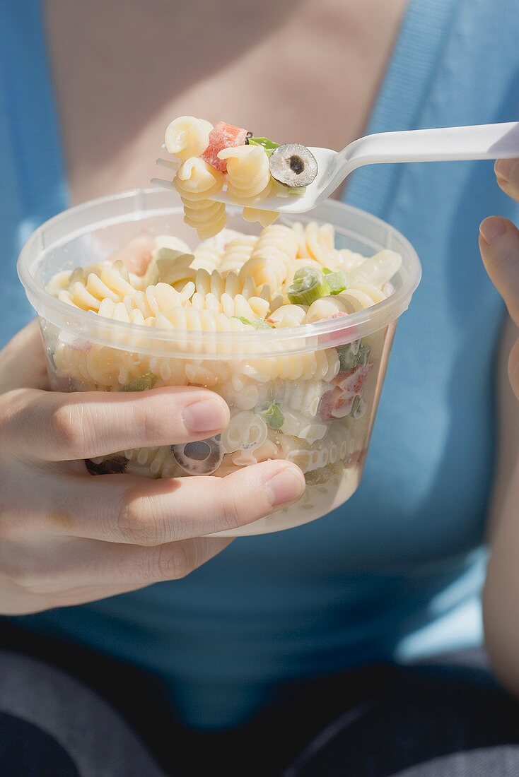 Frau isst Nudelsalat aus Plastikschale
