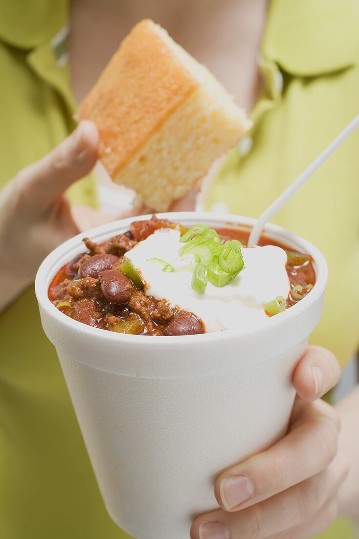 Woman holding chili con carne in paper cup and cornbread