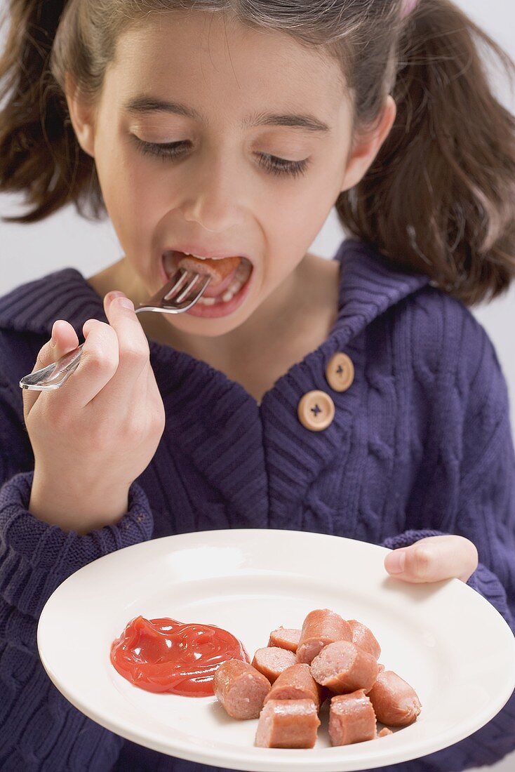 Kleines Mädchen isst Wiener Würstchen mit Ketchup