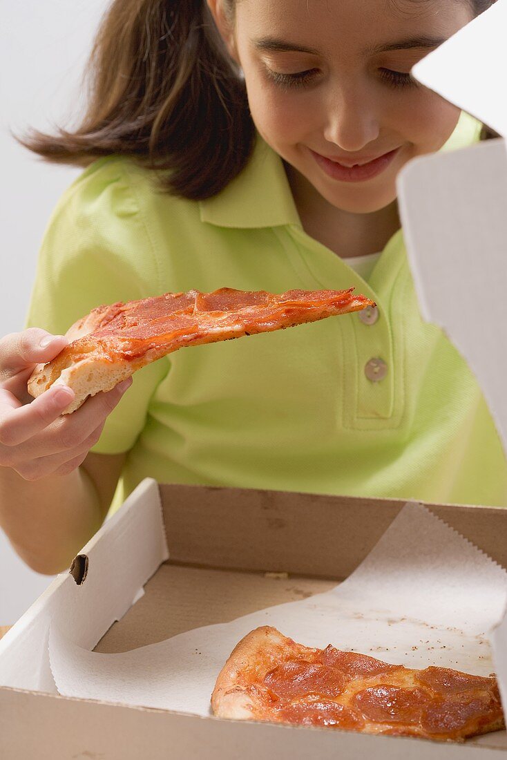 Kleines Mädchen hält Pizzastück über Pizzakarton