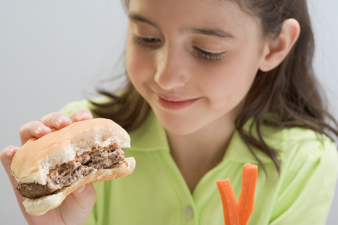 Kleines Mädchen hält angebissenen Hamburger und Möhrenstifte