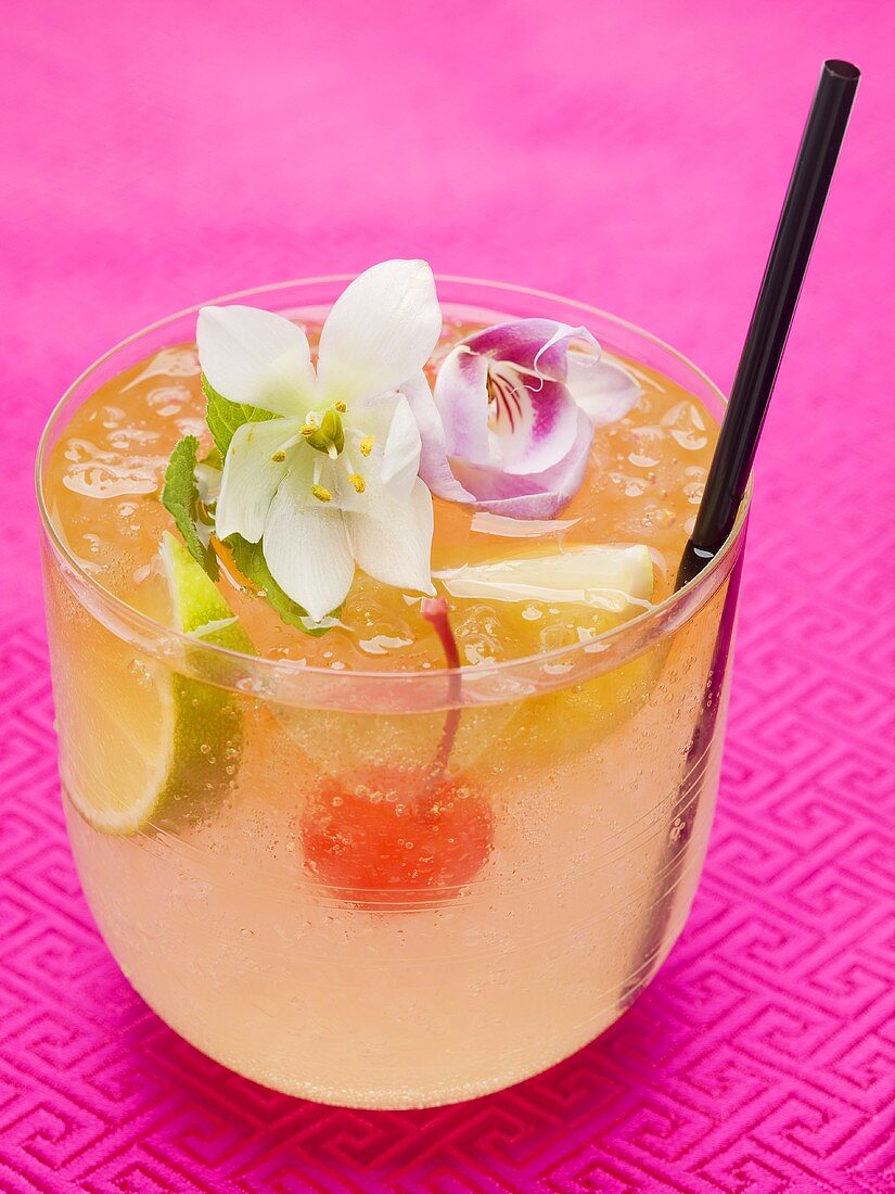 Drink mit Limetten, Cocktailkirsche und exotischen Blüten