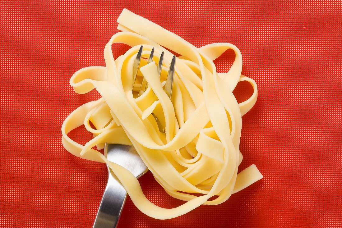Ribbon pasta wrapped around fork on red background