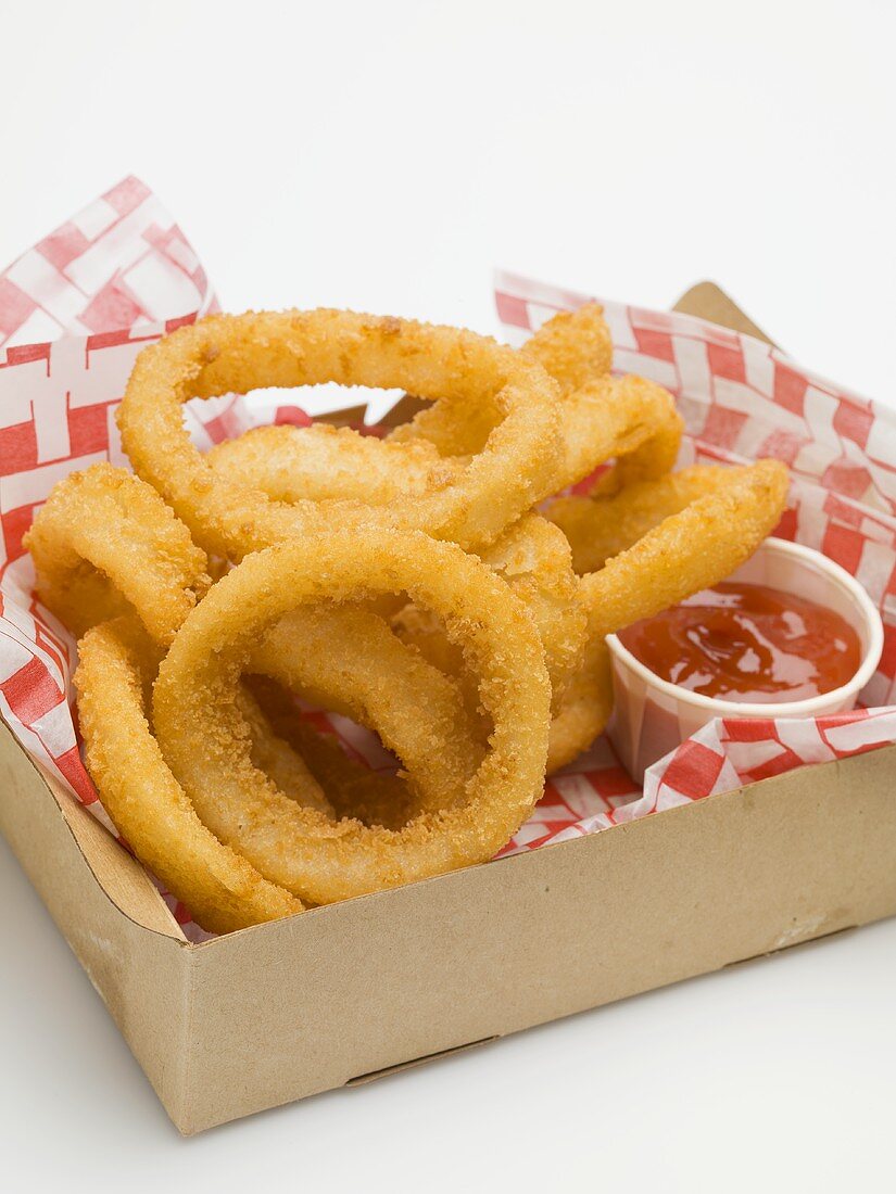 Deep-fried onion rings with ketchup in a cardboard box
