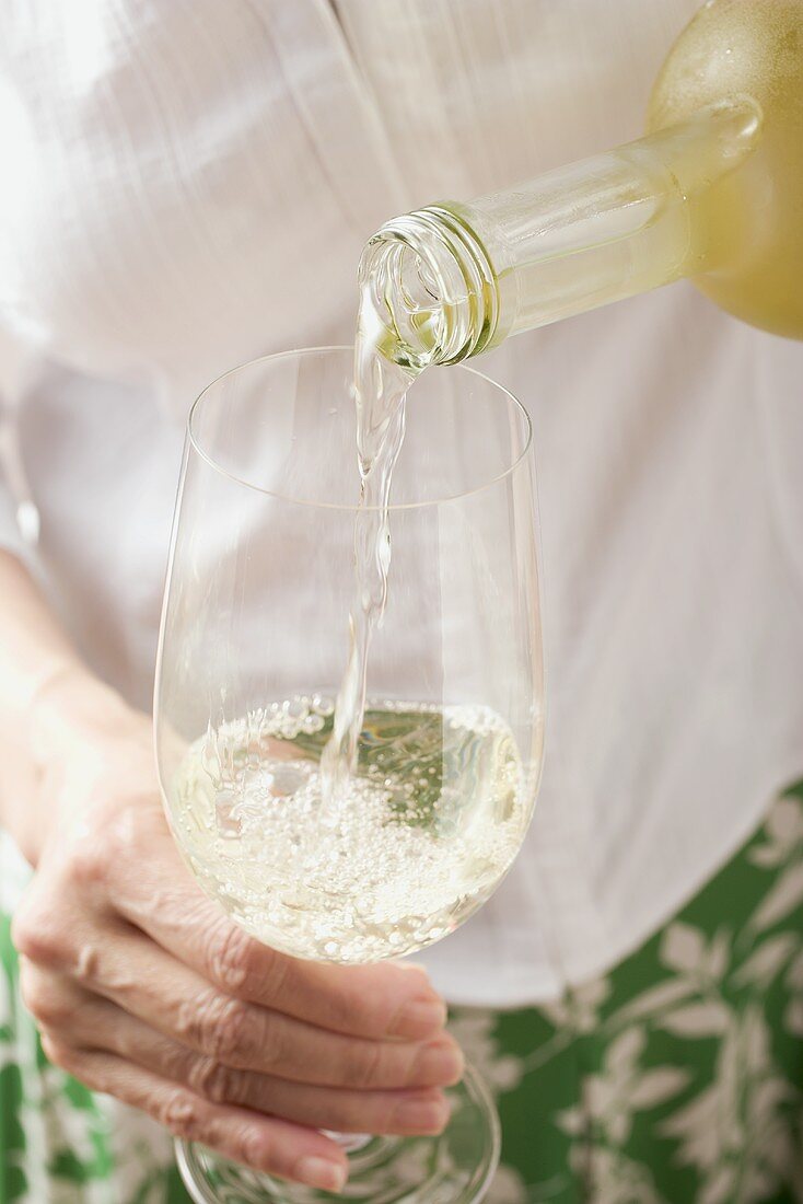 Frau schenkt Weißwein in Glas ein