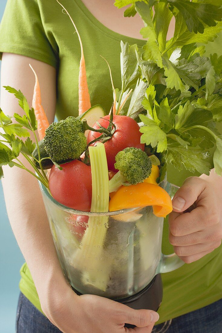 Frau hält frisches Gemüse und Kräuter im Mixer