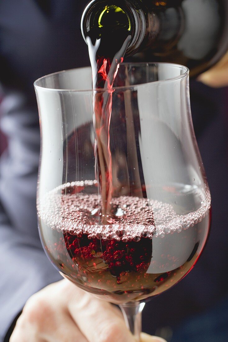 Person schenkt Rotwein in Glas ein