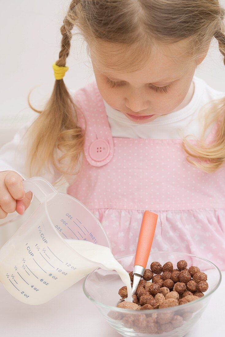 Kleines Mädchen giesst Milch auf Cerealien