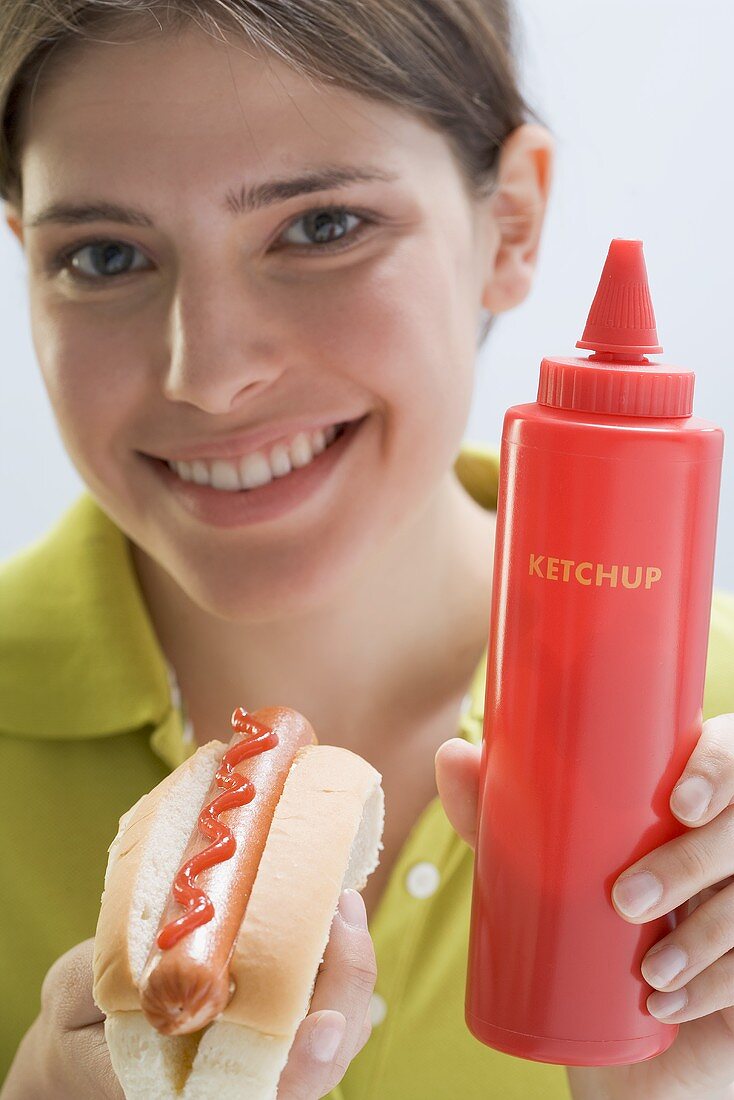 Young woman holding hot dog and ketchup bottle